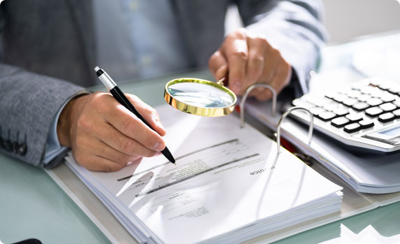 A person holding a magnifying glass over a document - Vision Law®