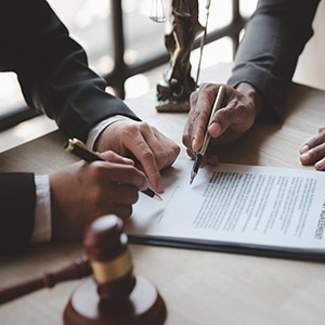 Two people in suits reviewing and signing a legal agreement or contract on a desk with a gavel